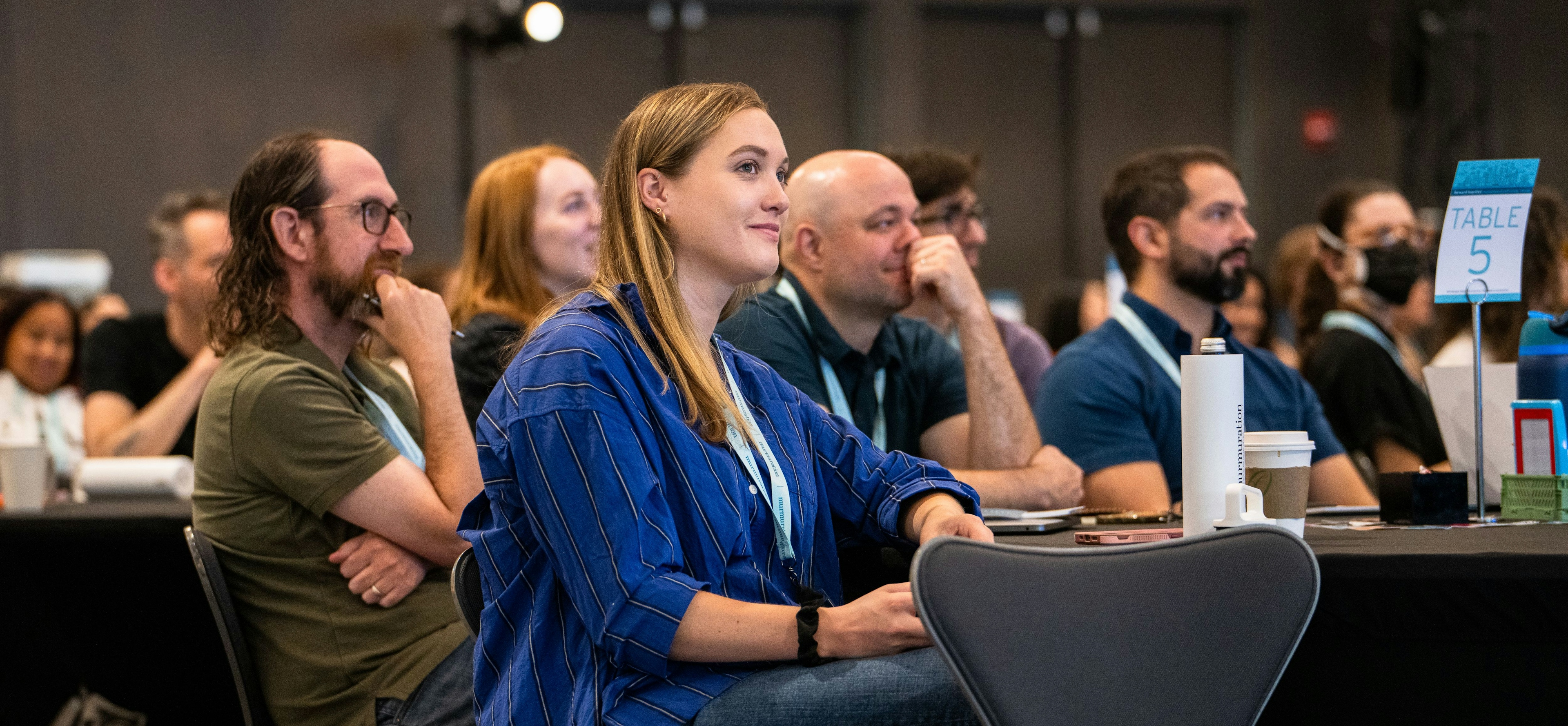 A crowd of people sit in an event ballrom and listen to a speaker. 